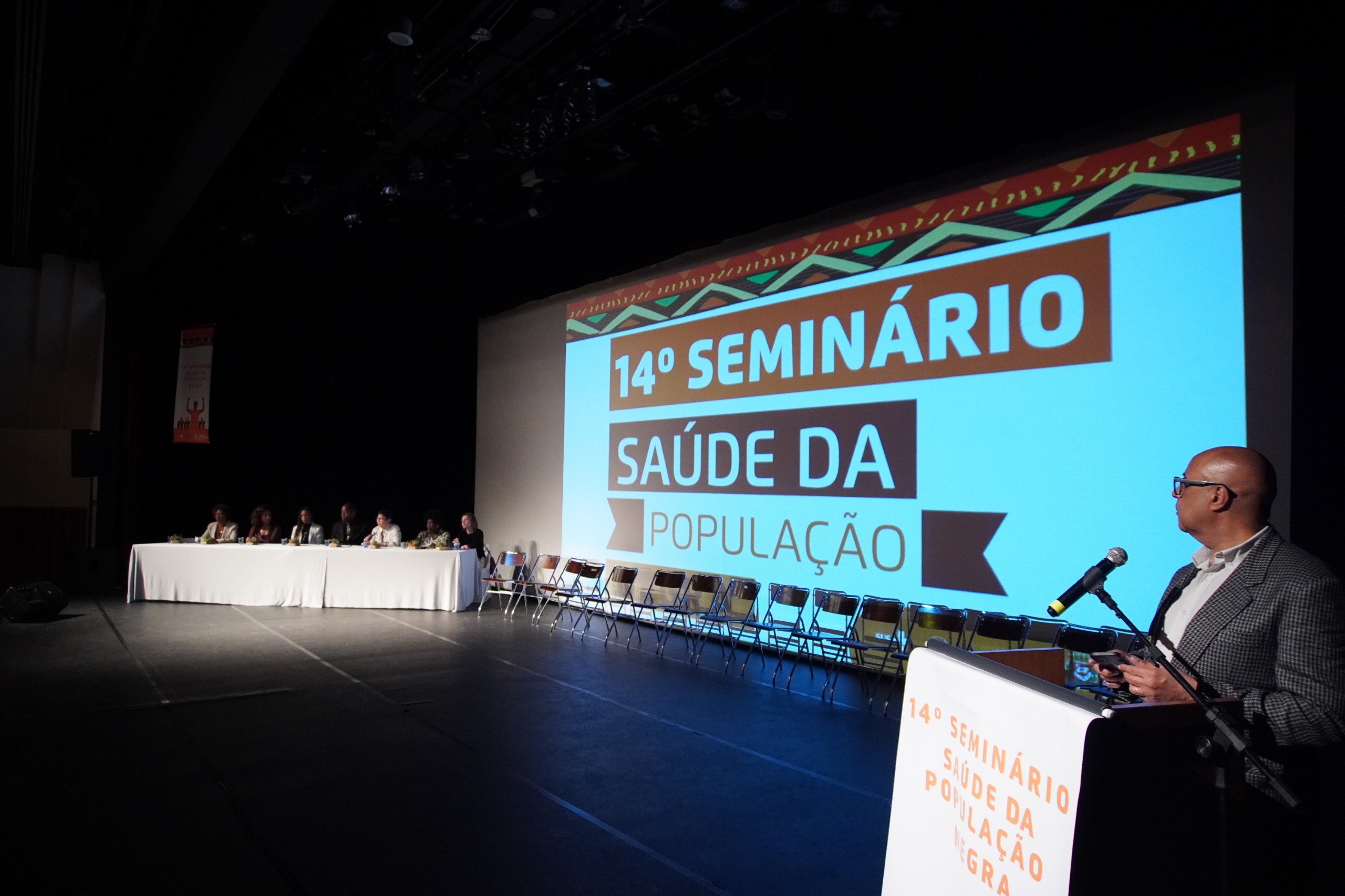 A imagem mostra um evento realizado em um auditório para o 