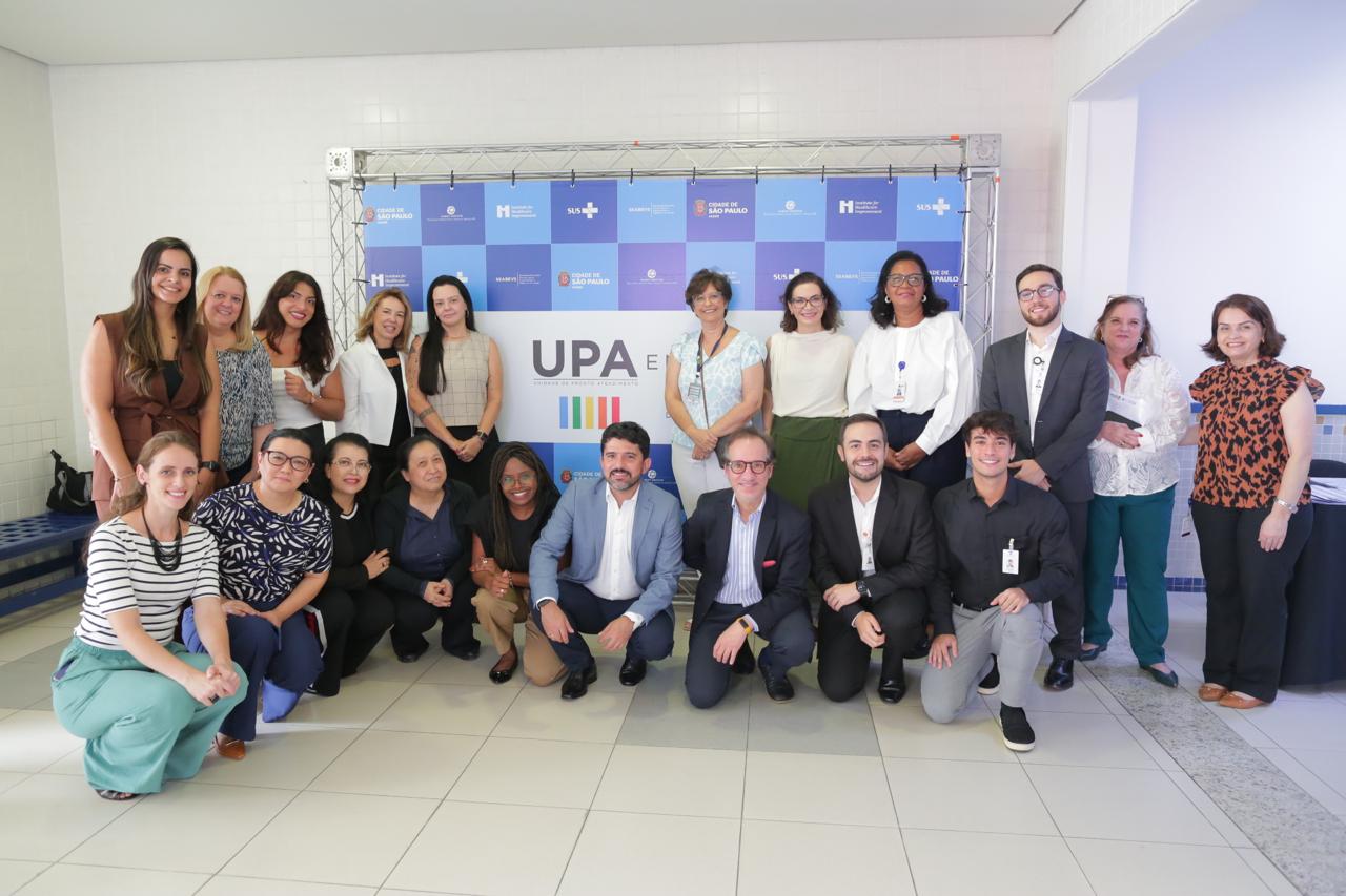 A imagem mostra um grupo de pessoas reunidas para uma foto em frente a um painel com o logotipo