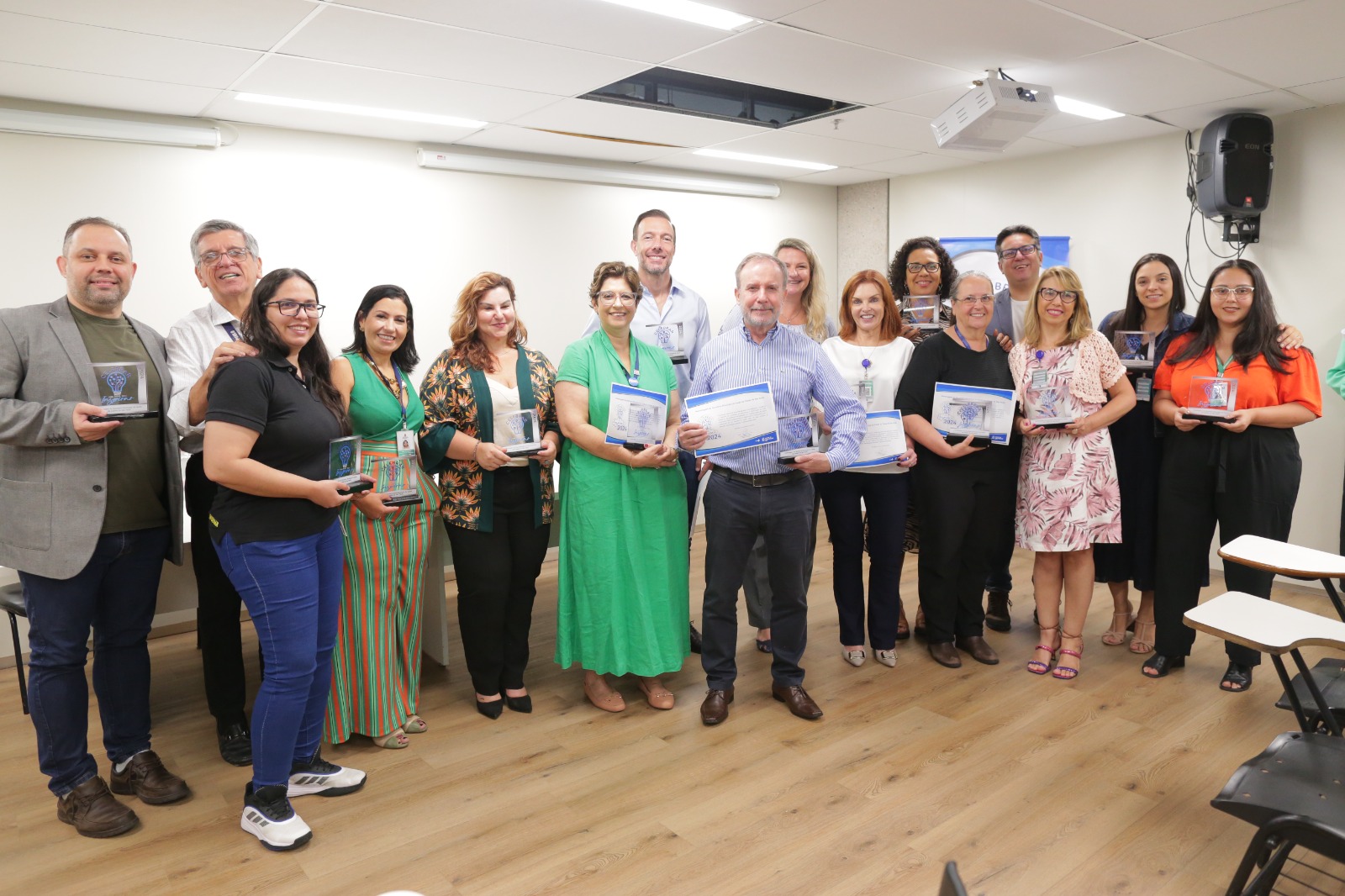 A foto mostra gestores da saúde segurando o prêmio de reconhecimento em formas de troféu e diploma. São homens e mulheres e todos estão sorrindo.