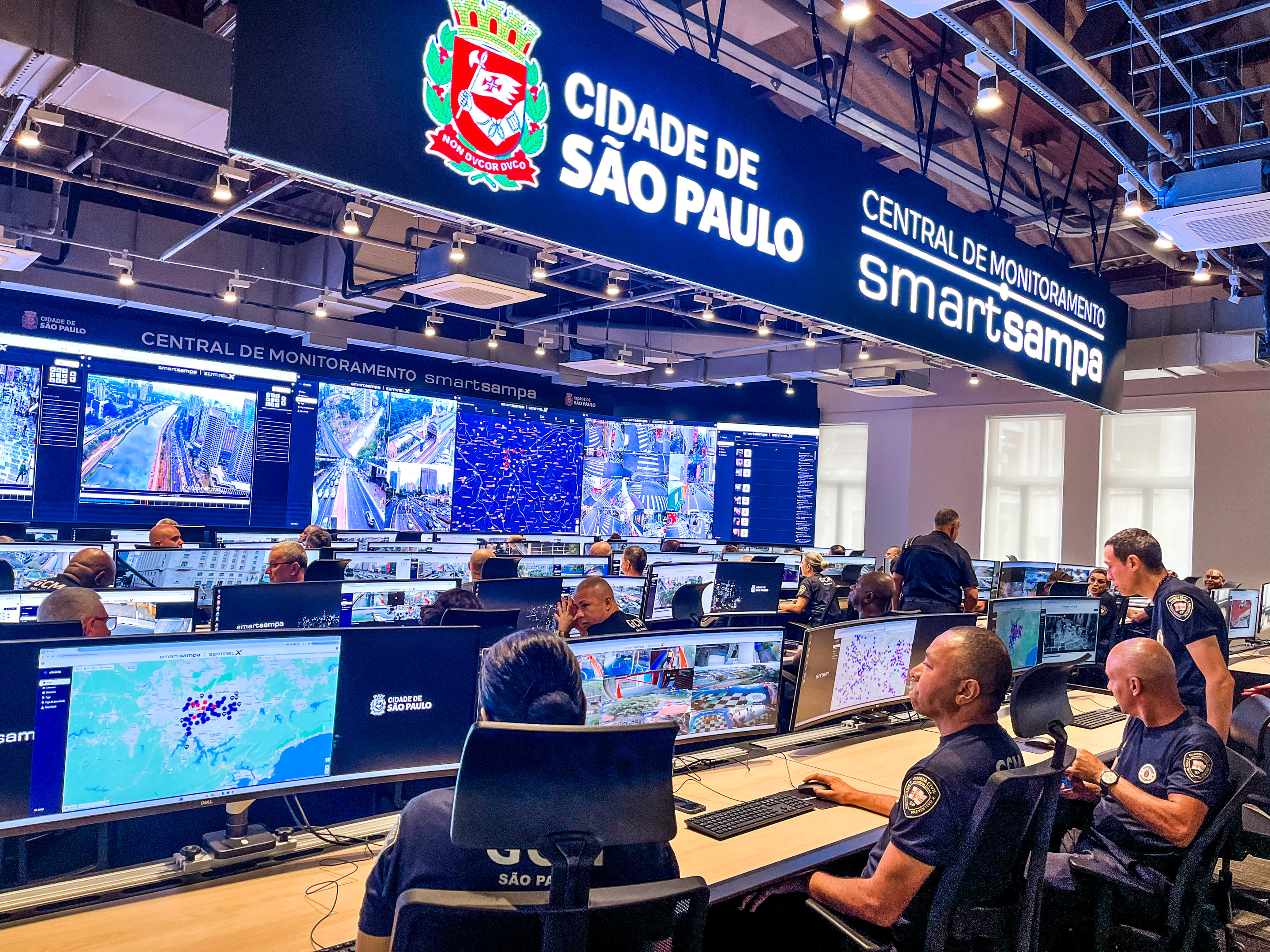 Foto mostra Central do SmartSampa com guardas sentados em frente a monitores e telões com imagens de dados, imagens da cidade e mapas.