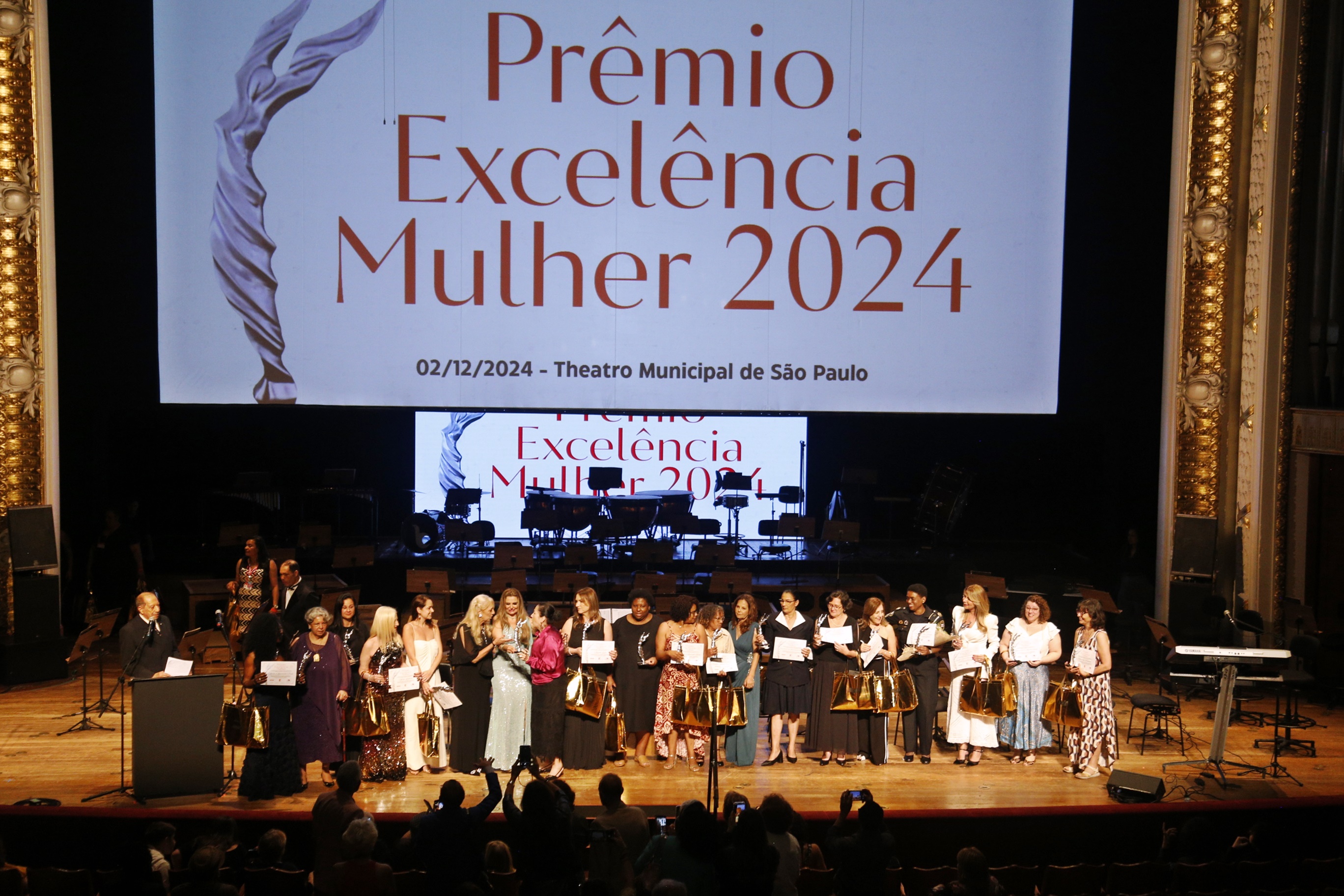 #PraTodosVerem A imagem mostra mulheres reunidas em um palco com diplomas nas mãos