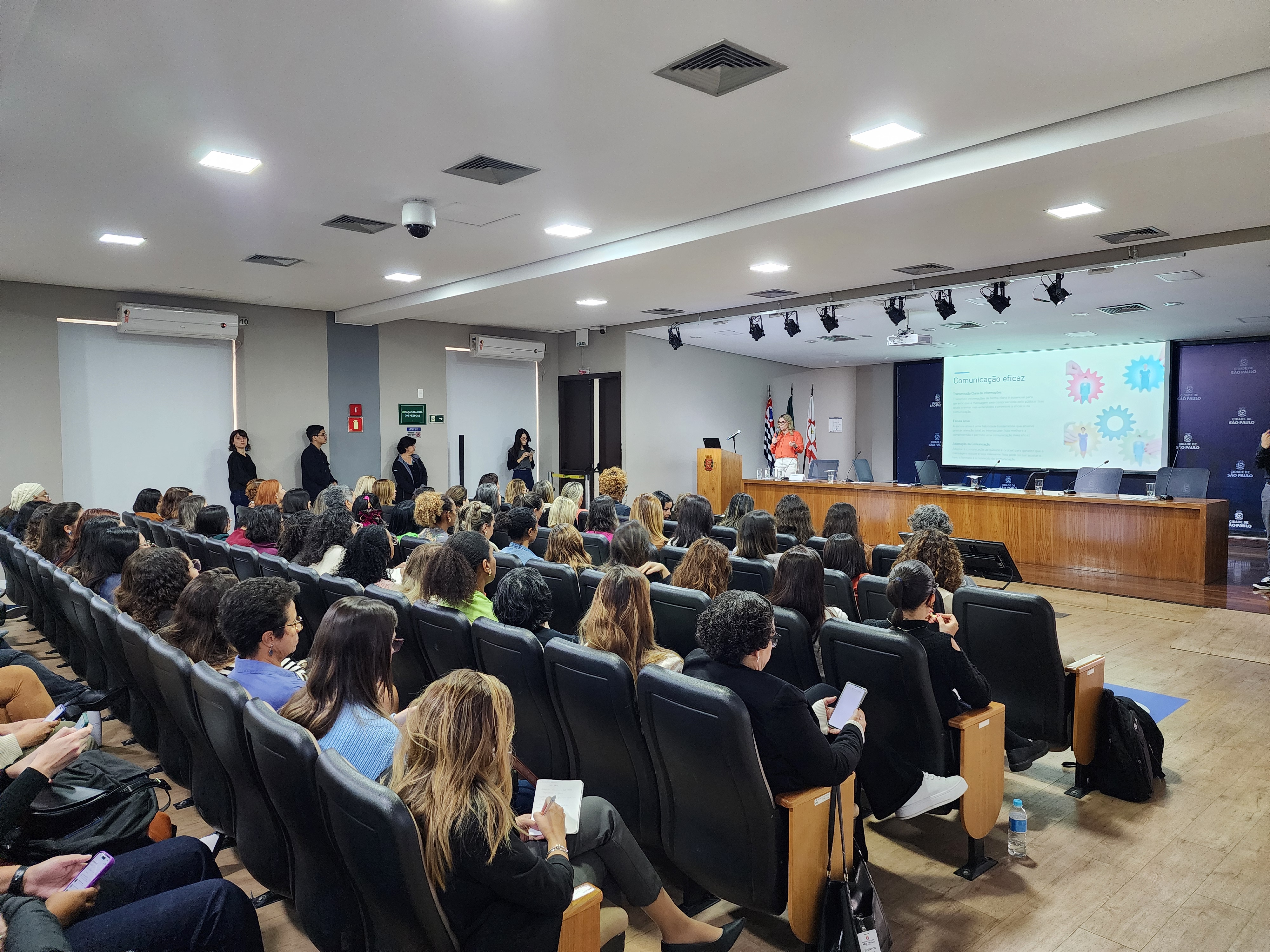 sala com várias pessoas sentadas. Um telão e uma apresentadora. Alessandra Karine vice-presidente da Microsoft