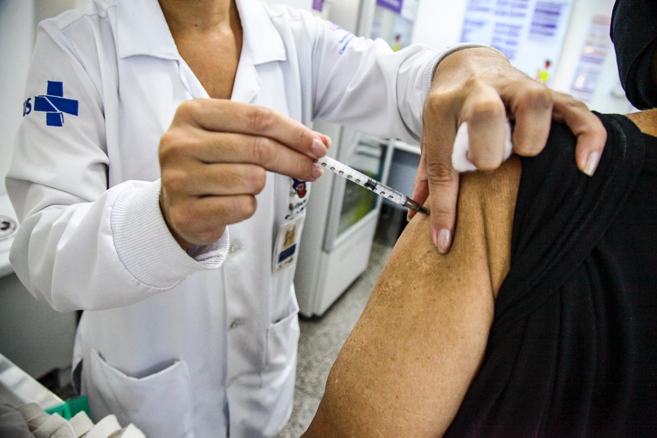 Imagem mostra profissional da saúde aplicado vacina em uma mulher. Imagem não mostra rostos 