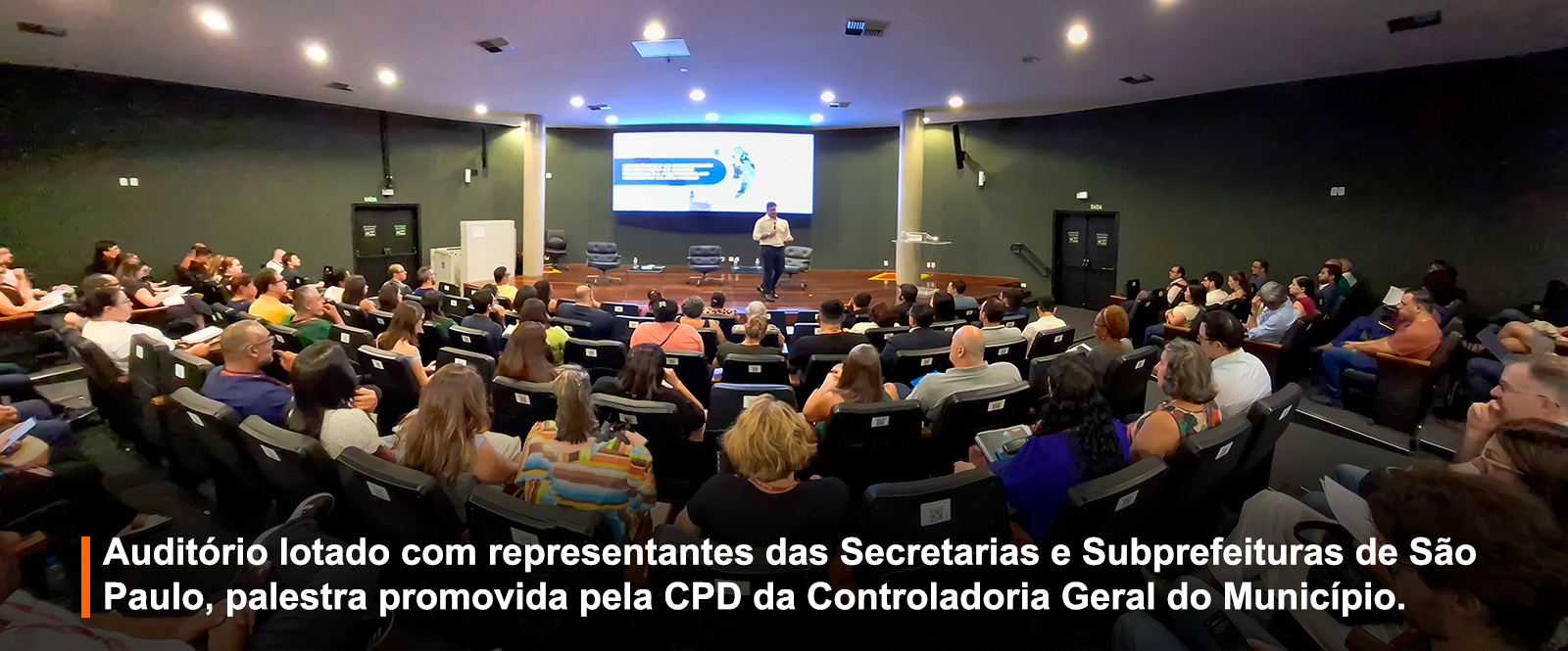 Foto registrada no auditório do TCM-SP, todos os acentos estão ocupados e o palestrante no centro da imagem 