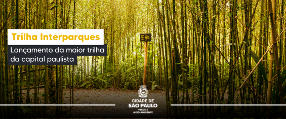 Imagem de fundo com uma área verde, repleta por plantas e bambus e com solo não pavimentado, de terra vermelha. No centro, há uma placa indicando um caminho, na direção direita. No centro inferior da imagem, há o logo da Secretaria do Verde e do Meio Ambiente com os seguintes dizeres: 