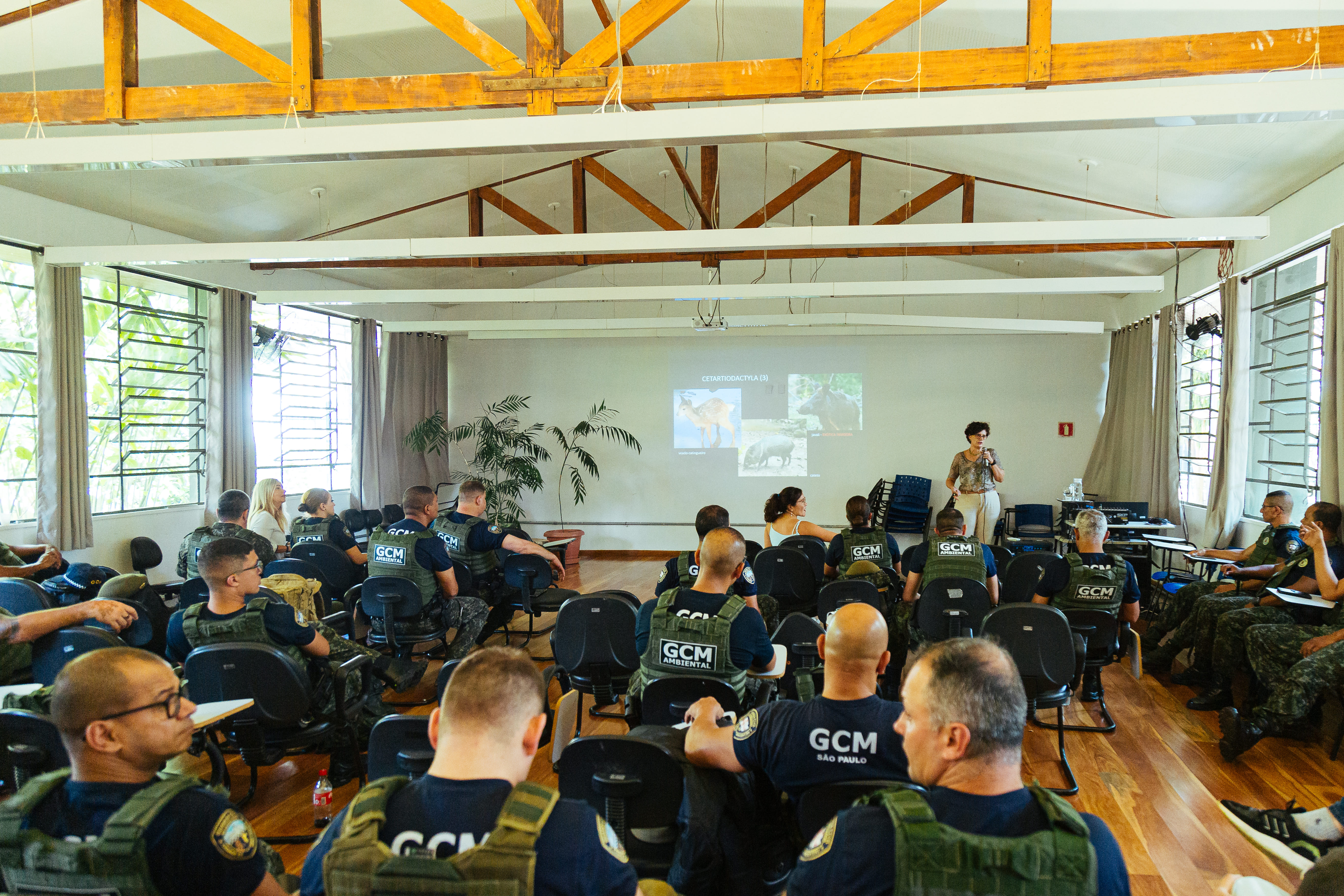 Indivíduos da Guarda Civil Metropolitana sentados em cadeiras, em sala de aula, durante o Curso de Fiscalização Ambiental. 