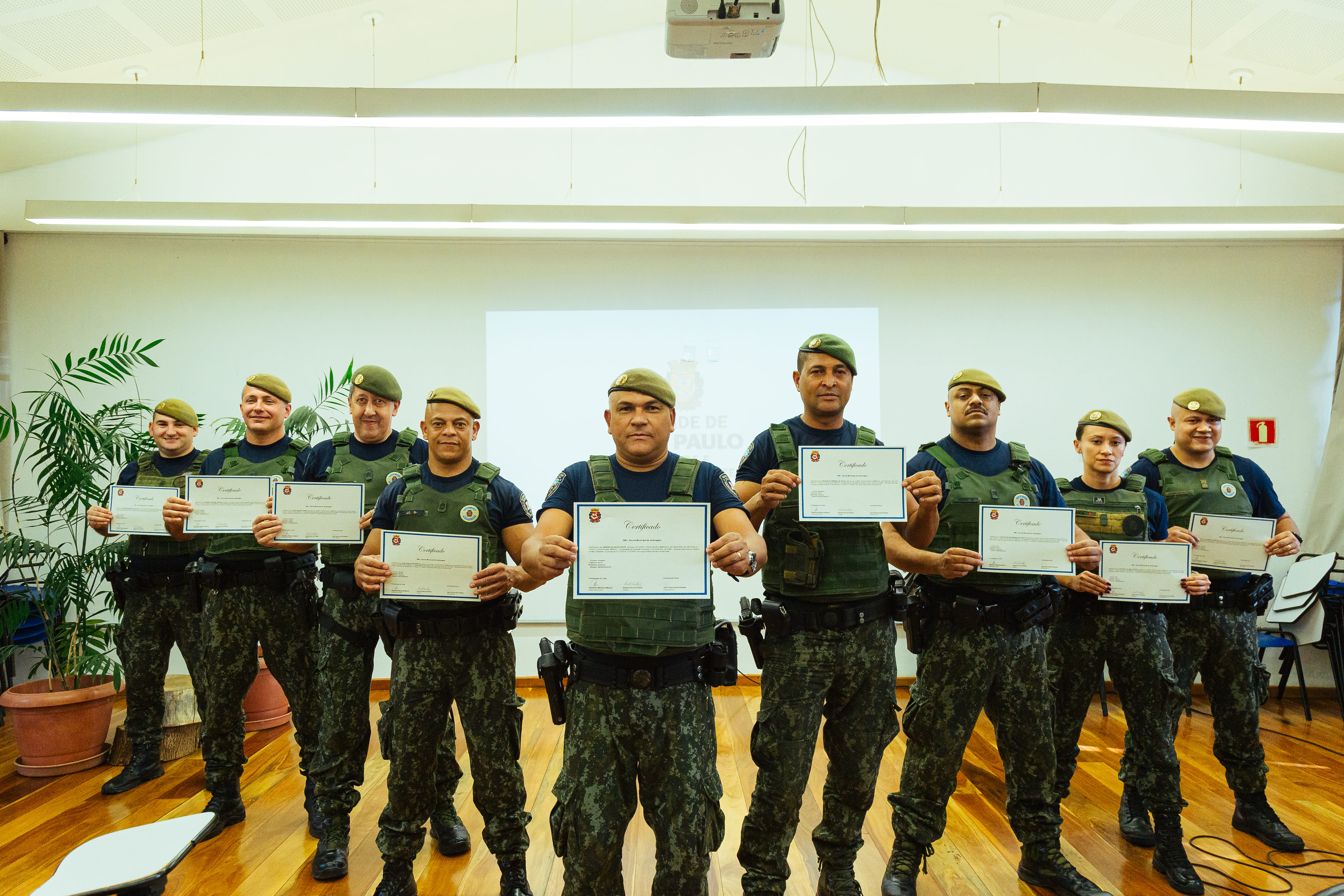 Indivíduos da Guarda Civil Metropolitana em fileira, vestidos com farda, posando para foto enquanto seguram o seu certificado de conclusão do Curso de Fiscalização Ambiental. 