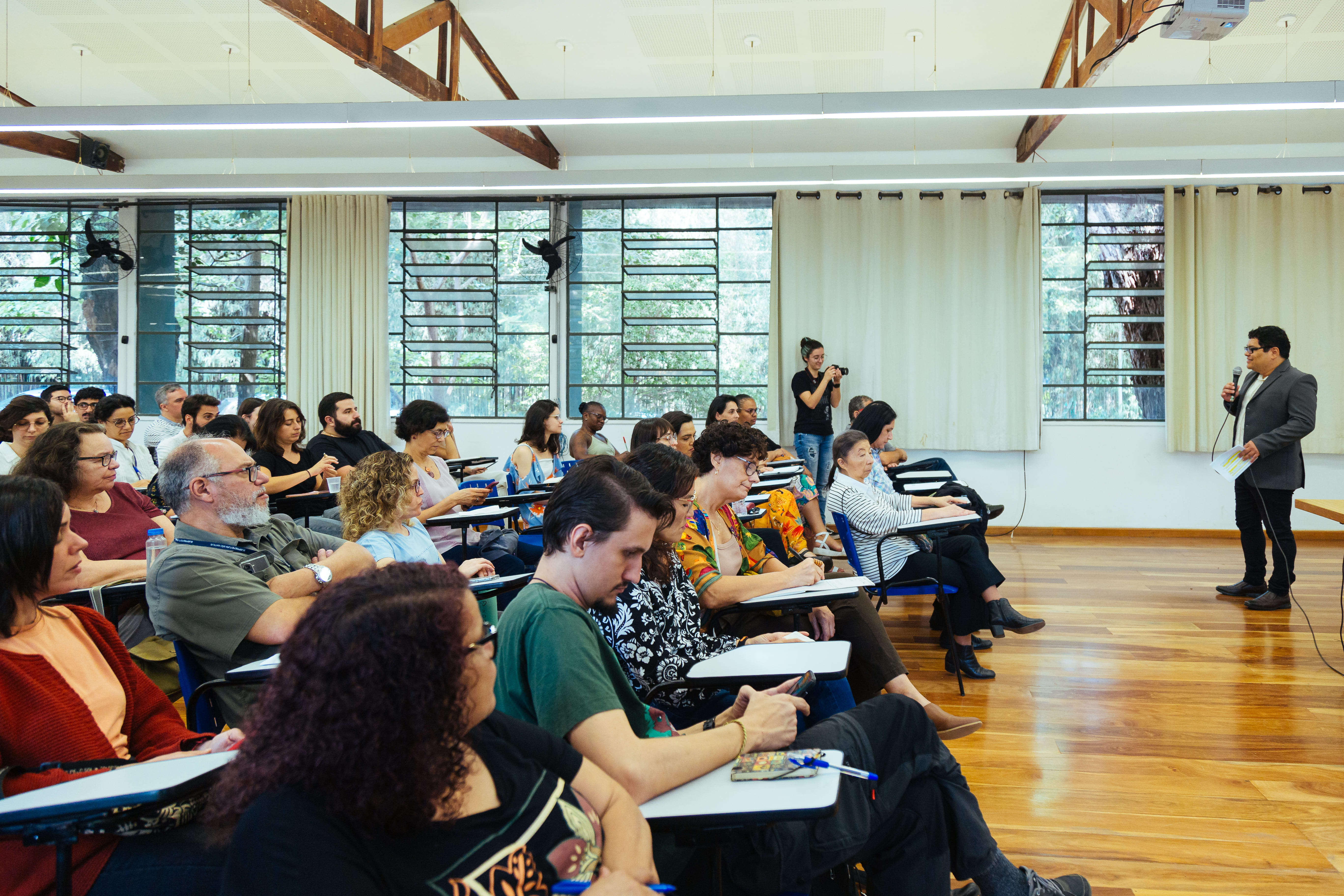 Palestrante  a frente dos convidados que estão sentados na sala do seminário