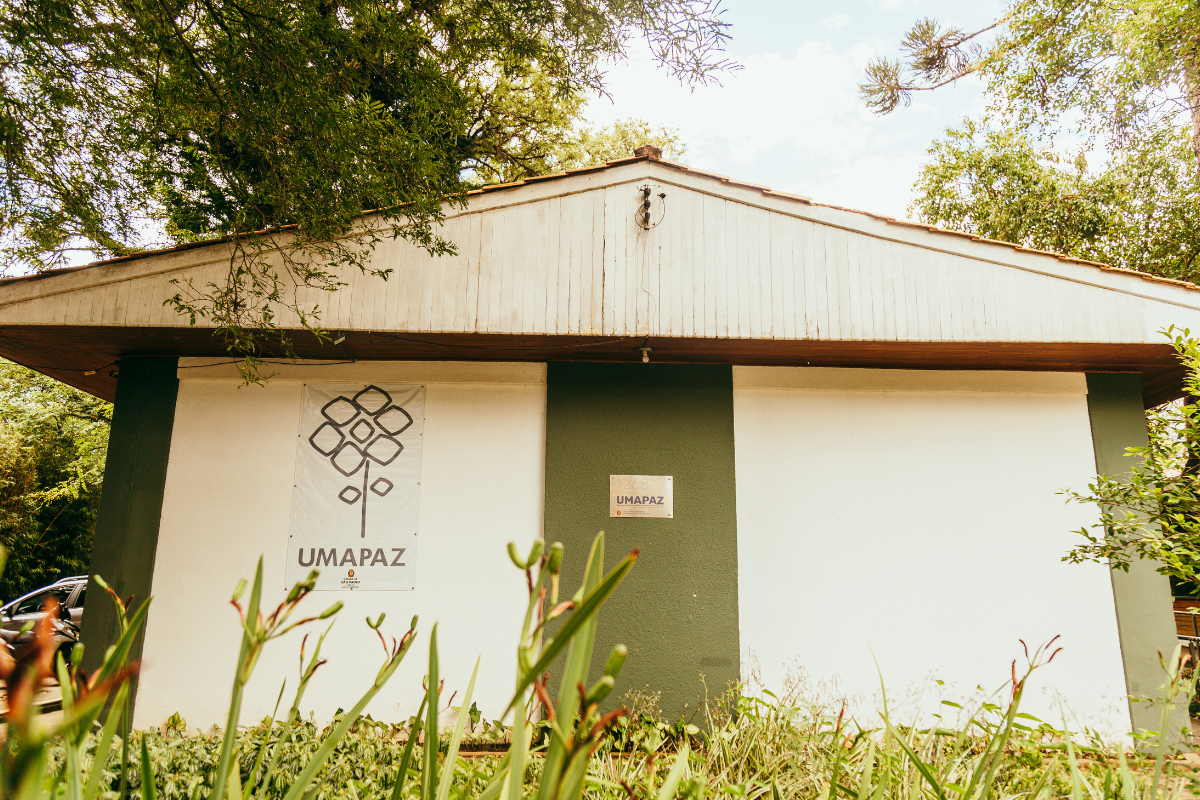 Fachada da sede da UMAPAZ (Universidade Aberta do Meio Ambiente e da Cultura de Paz), localizada no Parque Ibirapuera, em São Paulo. Em meio à vegetação, o prédio simples em tons verde e branco carrega o símbolo da instituição, que promove educação ambiental e ações pela cultura de paz.