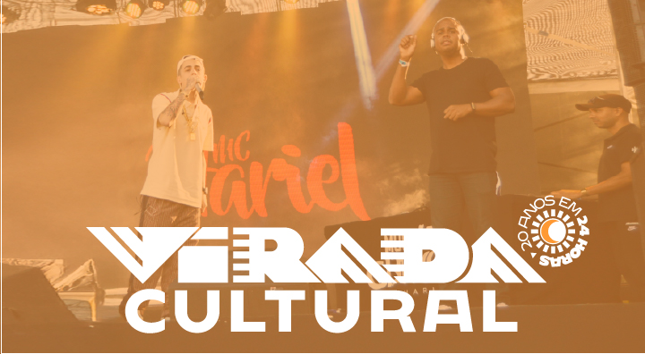 Fotografia captada durante o show do Mc Hariel, ao lado dele está um intérprete de Libras. Há um filtro de cor laranja com o texto: 20 anos em 24 horas. Virada Cultural.