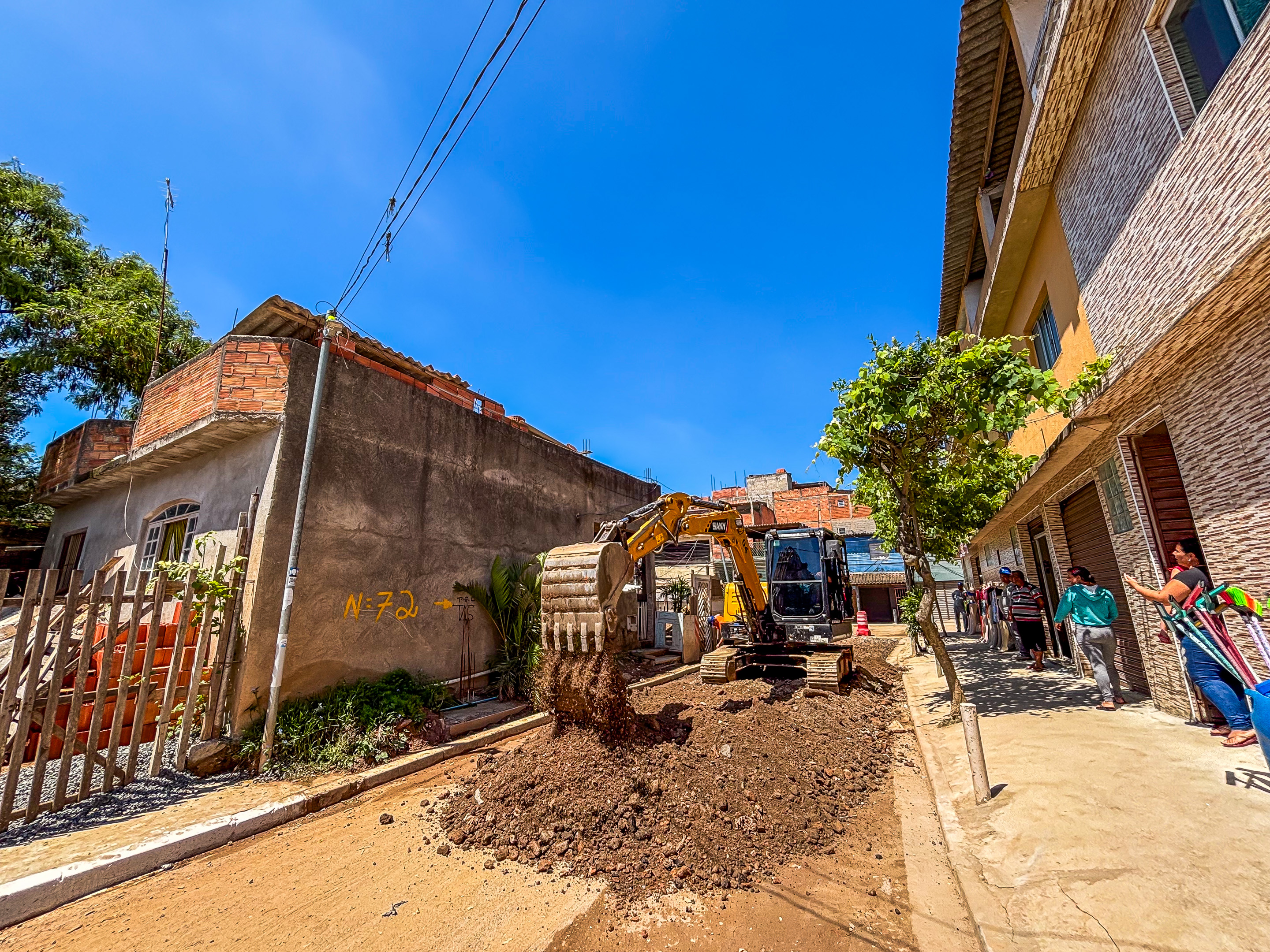 Rua Pedro de Medeiros em processo de pavimentação, estrada de terra. Na imagem há também uma escavadeira