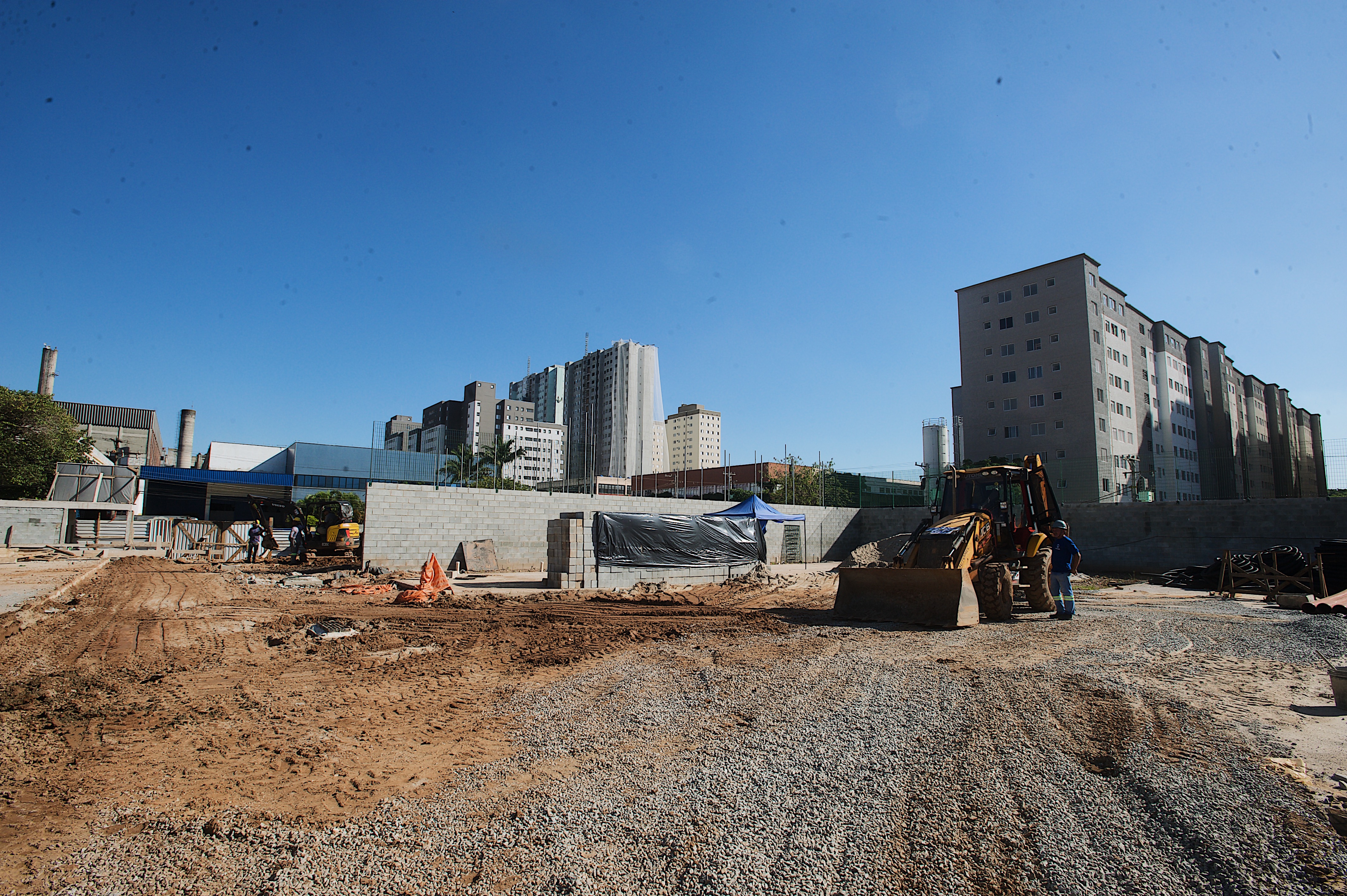 Espaço aberto com construção de fundo e máquina escavadeira. Chão de terra e pedra