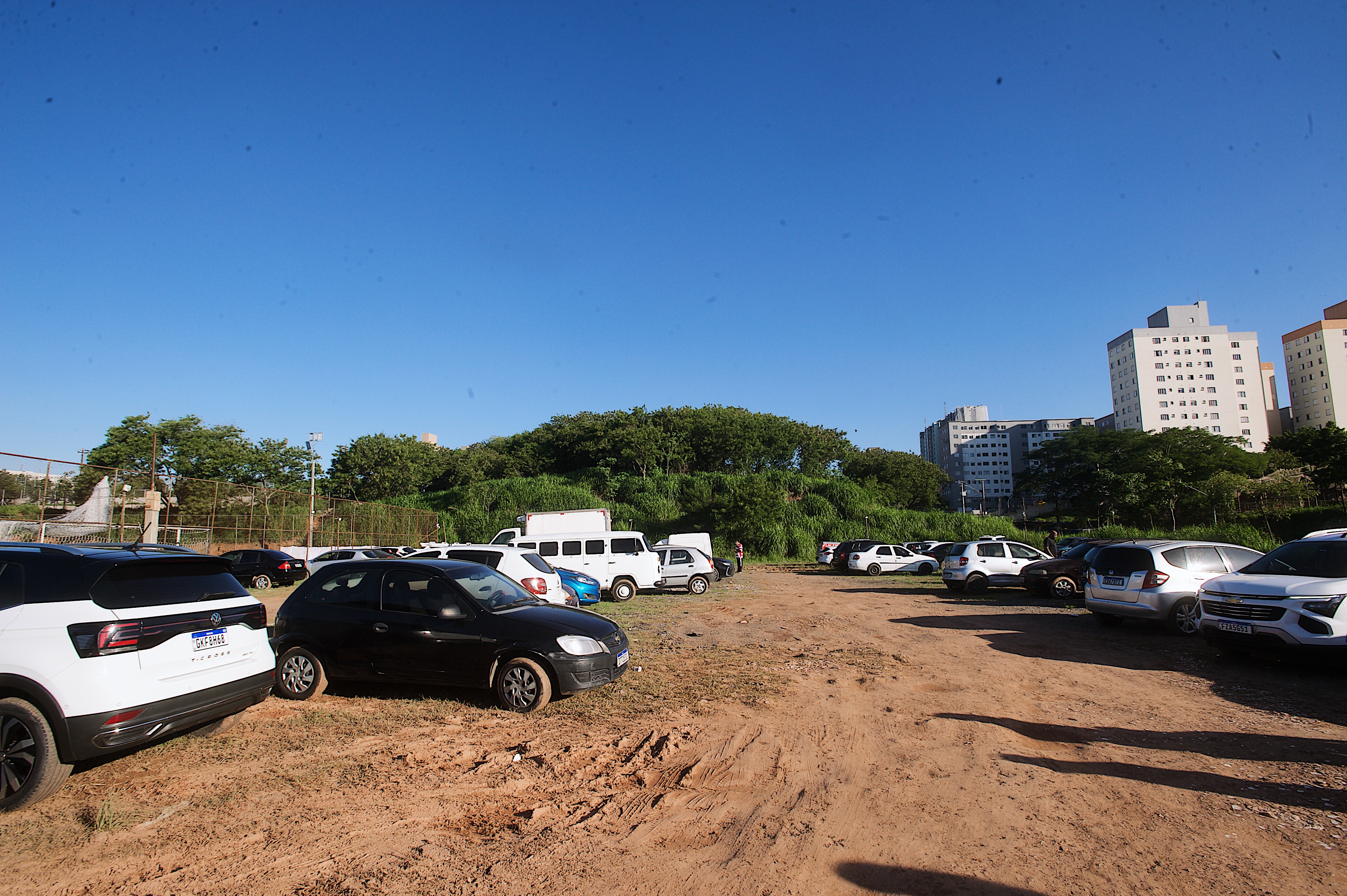Espaço aberto com carros estacionados, chão de terra.