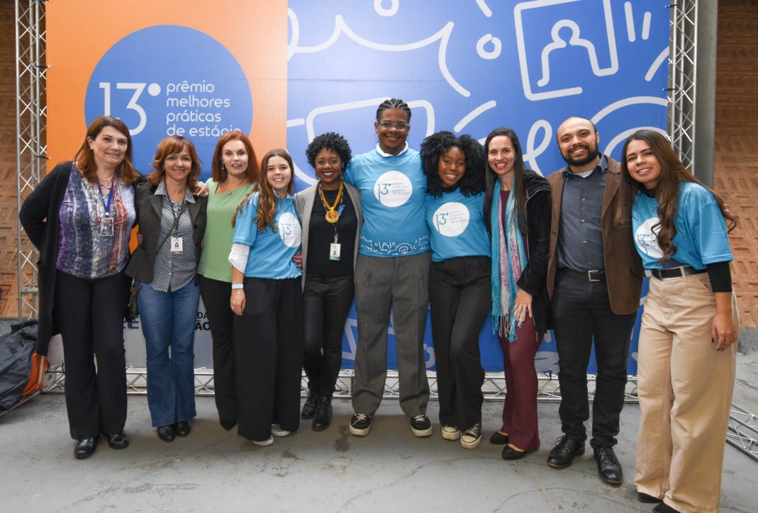 Na imagem estão dez pessoas em pé, uma ao lado da outra. Os três estagiários premiados estão no meio. Todos estão sorrindo. 